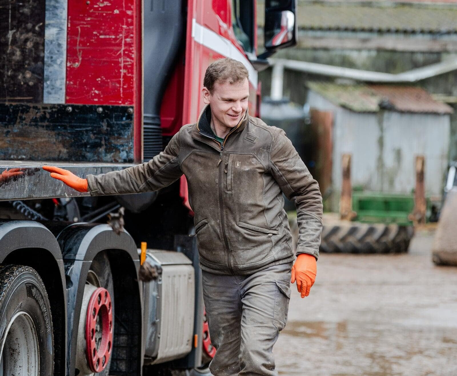 Farmer wearing protective clothing and gloves walking beside a commercial farm vehicle.
